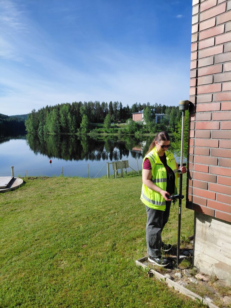 Alvan kesätyöntekijä tekemässä mittausta rakennuksen kulmalla.